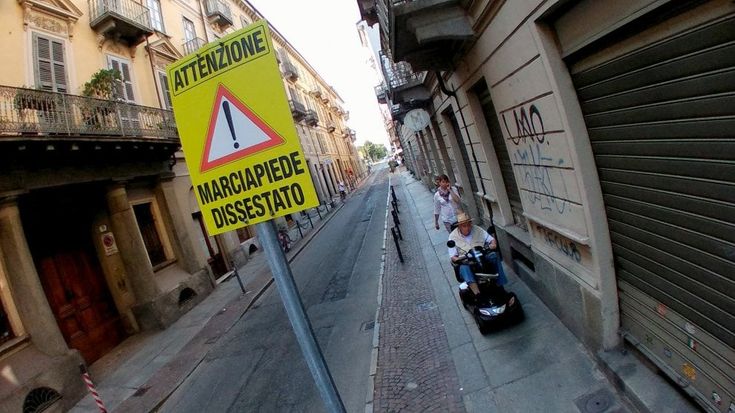 Sulle strade del centro un cartello avverte:"Attenzione marciapiede dissestato"